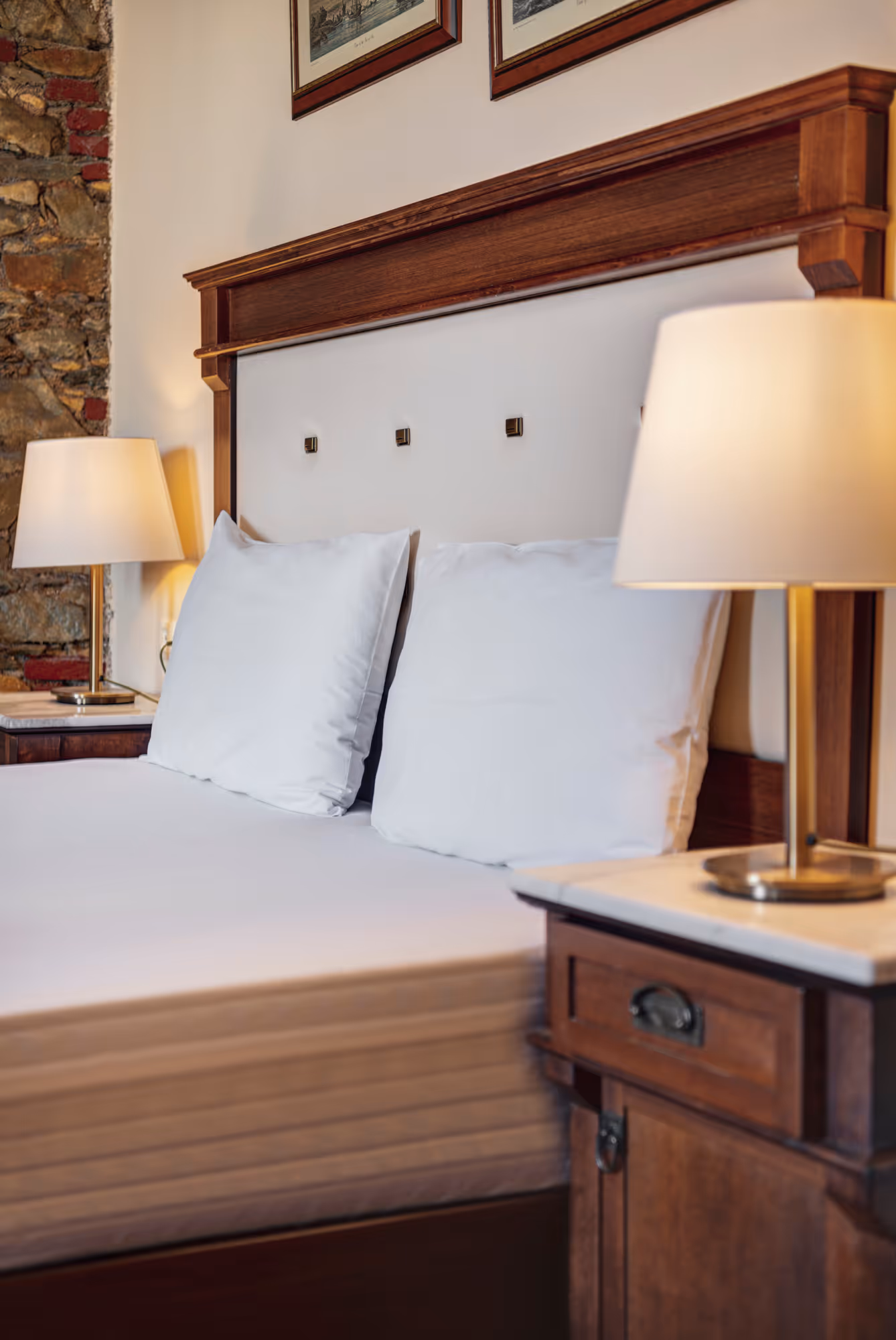 Close-up of a neatly made bed with white pillows and wooden headboard in a cozy room with table lamps on wooden nightstands.